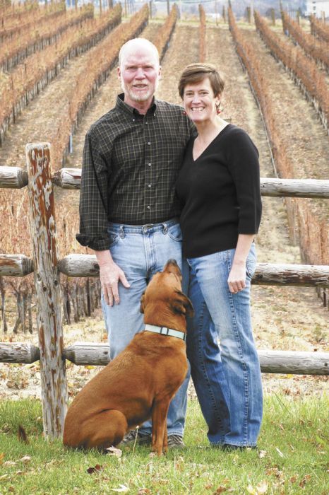 Patrick Flannery and Paula Brown stand in front of estate vines with their 7-year-old vineyard pooch, Vino.